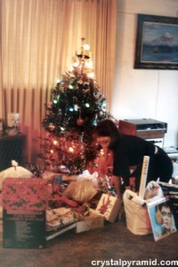 Patty Mooney in front of living Christmas tree laden with presents, 1983