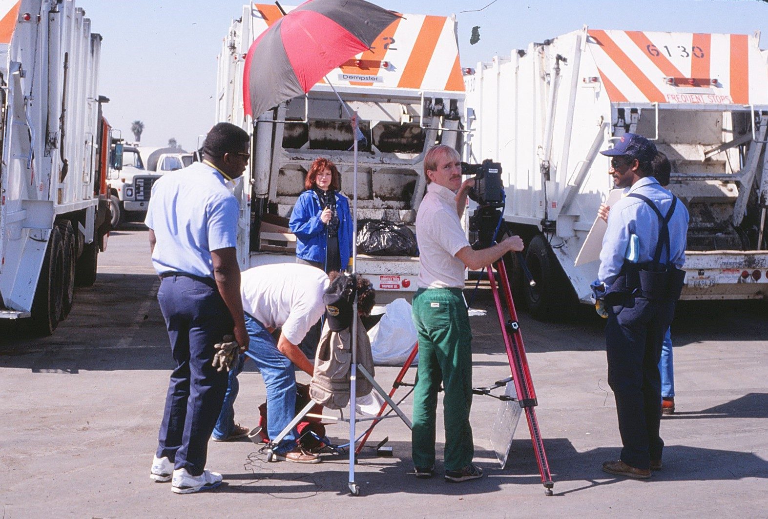 Mark Schulze filming an on-camera host in front of garbage trucks with sanitation workers for the 1988 video Get Smart About Toxics
